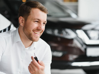 Happy buyer holding keys near the car in front of the modern avtosalon building