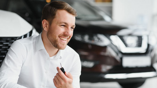 Happy buyer holding keys near the car in front of the modern avtosalon building