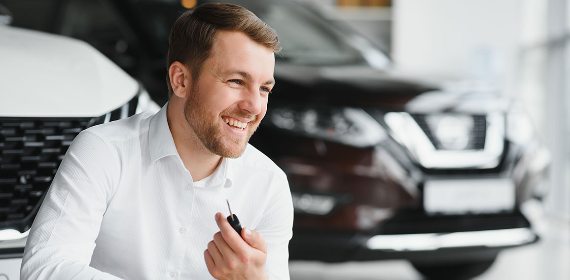 Happy buyer holding keys near the car in front of the modern avtosalon building
