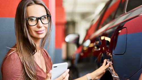 Portrait of young woman with scratched car at underground parking lot