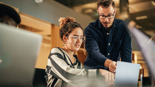 Two Colleagues Working On Laptop in Office. Female Hispanic Help