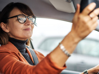 Adult caucasian businesswoman in glasses adjusting the rearview mirror while sitting at the wheel of a car