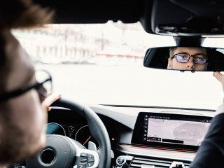 Young businessman driving alone adjusting rearview mirror