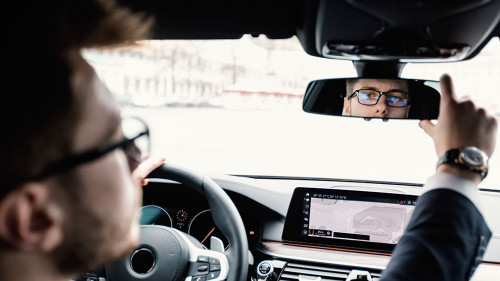 Young businessman driving alone adjusting rearview mirror