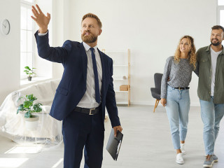 Real estate agent giving happy young customers a tour about a new spacious house
