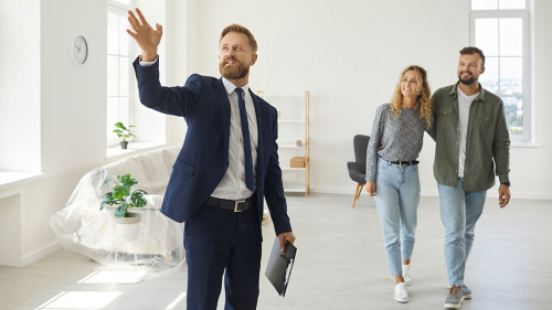 Real estate agent giving happy young customers a tour about a new spacious house