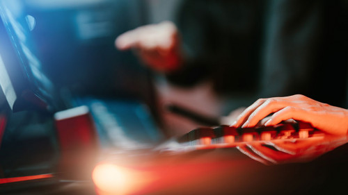 Hacker in dark room using keyboard stealing data on internet.