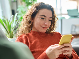 Smiling relaxed young woman sitting on couch using mobile phone technology.
