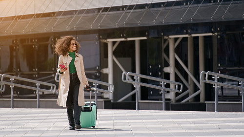 Young african woman walking outdoors carrying a suitcase and goi