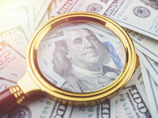 Closeup one hundred US dollar bills under gold magnifying glass