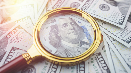 Closeup one hundred US dollar bills under gold magnifying glass