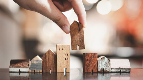 Hand choosing mini wood house model from model on wood table, se