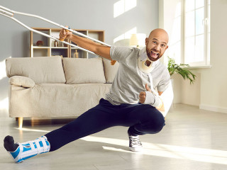 Happy man who's on sick leave due to his injuries is holding crutch and showing thumbs-up