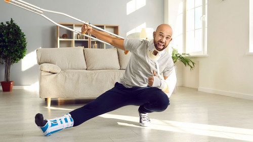 Happy man who's on sick leave due to his injuries is holding crutch and showing thumbs-up