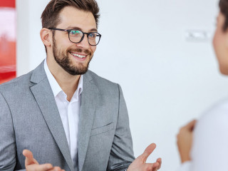 Smiling friendly car seller sitting in car salon with a woman wh