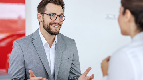 Smiling friendly car seller sitting in car salon with a woman wh