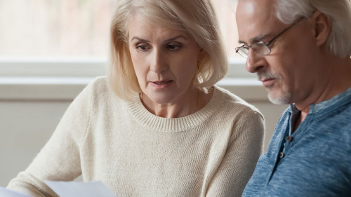 Aged couple read bank statement analyzing family expenses feels concerned