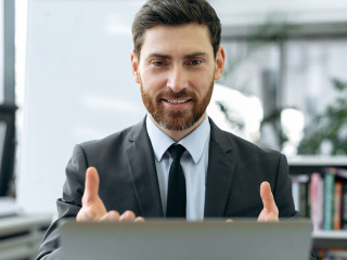 Concentrated caucasian businessman, information security engineer, insurance manager, sit in modern office, having video meeting with colleague using laptop, explaining working strategy,gestures hands