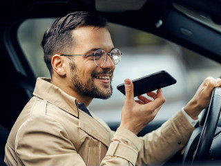 A happy businessman is driving his car and leaving voice massage