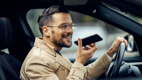 A happy businessman is driving his car and leaving voice massage