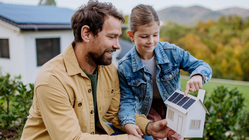Little girl with her dad holding paper model of house with solar panels, explaining how it works.Alternative energy, saving resources and sustainable lifestyle concept.