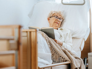 Sick senior woman lies in a hospital bed and reads a book