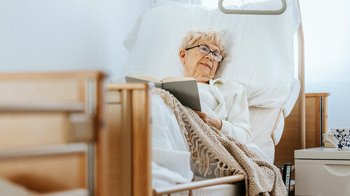 Sick senior woman lies in a hospital bed and reads a book