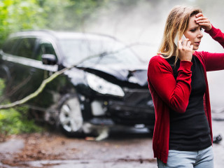 A young woman with smartphone by the damaged car after a car accident, making a phone call.