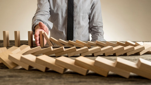 Hand stopping domino effect of wooden blocks