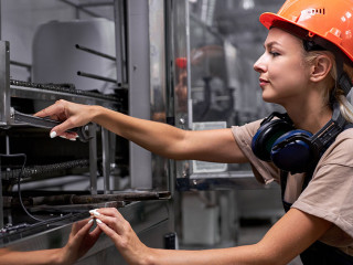 Serious female repairing broken equipment in factory using wrench, in uniform
