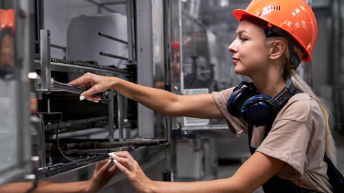 Serious female repairing broken equipment in factory using wrench, in uniform