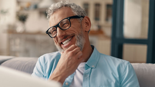 Cheerful senior man in casual clothing and eyeglasses using lapt