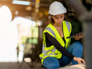 Young female in protective uniform inspecting industrial machine