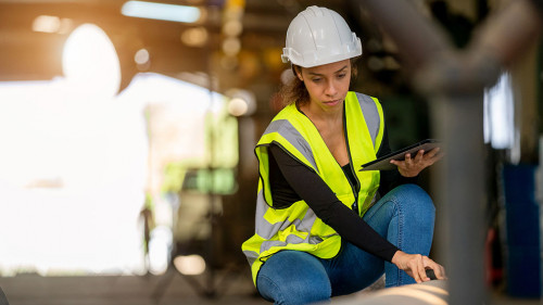 Young female in protective uniform inspecting industrial machine