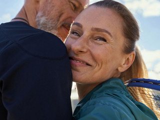 Portrait of active mature couple looking happy while embracing each other outdoors, ready for morning workout on tennis court