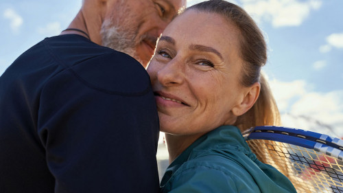Portrait of active mature couple looking happy while embracing each other outdoors, ready for morning workout on tennis court
