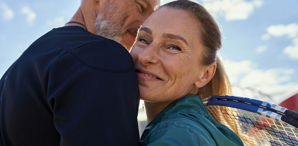 Portrait of active mature couple looking happy while embracing each other outdoors, ready for morning workout on tennis court