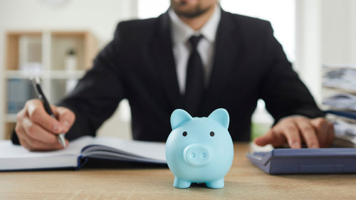 Piggy bank on desk of accountant who uses calculator to analyze budget and make calculations.