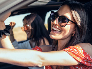 Pretty young women singing while driving a car on road trip on b