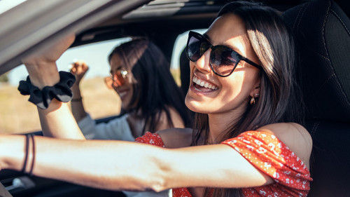 Pretty young women singing while driving a car on road trip on b