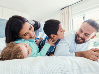 Happy, love and family being playful on the bed together in the bedroom of their modern house. Happiness, excited and children having fun, playing and bonding with their parents in a room at home.