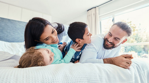 Happy, love and family being playful on the bed together in the bedroom of their modern house. Happiness, excited and children having fun, playing and bonding with their parents in a room at home.