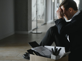 Sad fired businessman sitting outside meeting room after being dismissed.