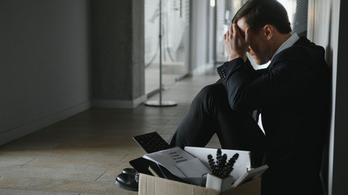 Sad fired businessman sitting outside meeting room after being dismissed.