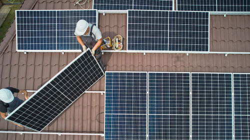 Men technicians mounting photovoltaic solar moduls on roof of house.