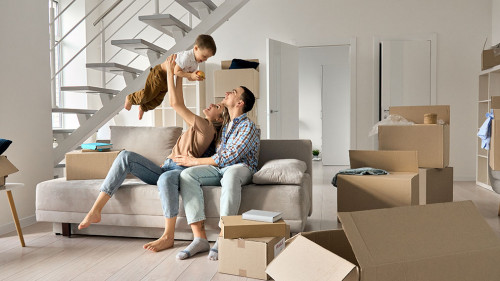 Happy young family playing with kid son together in new home on moving day.