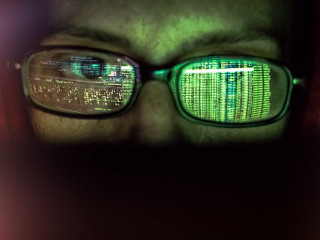hacker at computer data reflecting in eyeglasses