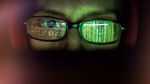 hacker at computer data reflecting in eyeglasses
