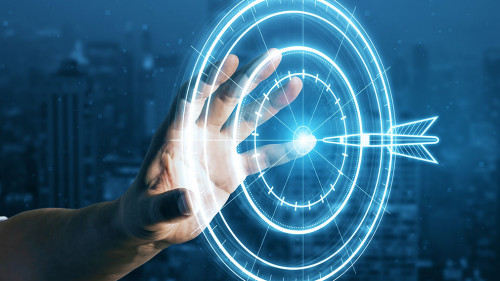 Target concept with a glowing hologram of bullseye and arrow hitting the center. Goals achievement, success. Close up of businessman hand using hud screen on blurry night city background.