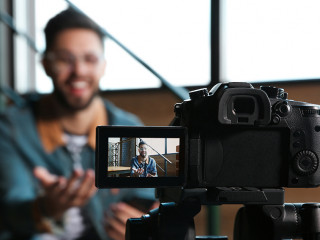 Young blogger recording video indoors, focus on camera screen